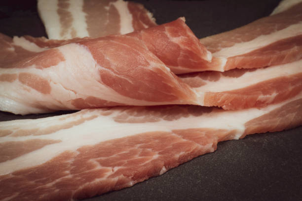 Raw dry-cured back bacon Close up raw dry-cured back bacon on a dark stone serving plate twisted bacon stock pictures, royalty-free photos & images