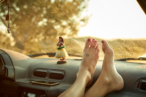 Close-up of woman's feet on dashboard. Low section of female is relaxing in mini van. She is on road trip.