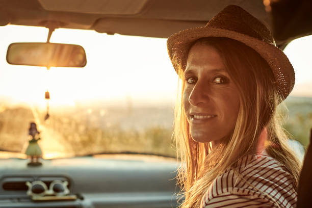 Portrait of woman wearing sun hat in mini van. Confident female is smiling during road trip. She is enjoying weekend during sunset.