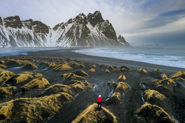 Mature woman exploring Stokksnes with Vestrahorn mountain in the background Mature woman exploring Stokksnes with Vestrahorn mountain in the background, Iceland. black sand stock pictures, royalty-free photos & images