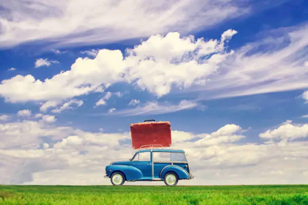 Photo of Old car with a suitcase on the trunk in the field against the blue sky with beautiful clouds. Copy space. Travel concept.