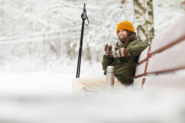 Woman in Winter Park Side view portrait of active young woman smiling at camera while enjoying hot cocoa sitting on bench in beautiful winter forest, copy space hot women working out pictures stock pictures, royalty-free photos & images