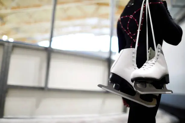 Closeup of unrecognizable girl holding figure skates over shoulder leaving ice rink after sports training, copy space