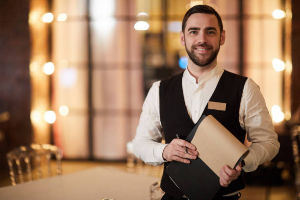 Profesional Waiter in Restaurant Waist up portrait of handsome waiter smiling cheerfully at camera standing in luxury restaurant or cafe, copy space waiter stock pictures, royalty-free photos & images