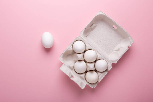 Six white eggs in carton box on pink paper background Top view Symbol Happy Easter Flat lay stock photo