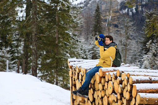 The photographer with camera is sitting on logs in winter mountains