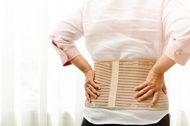 back pain, senior woman wearing back support belt on white background - bustiers imagens e fotografias de stock
