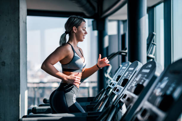 vue latérale de belle femme musculaire fonctionnant sur le tapis roulant. - salle de gym photos et images de collection