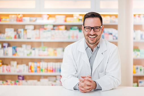 Retrato de un joven farmacéutico alegre apoyado en un mostrador en la farmacia, mirando a la cámara. photo