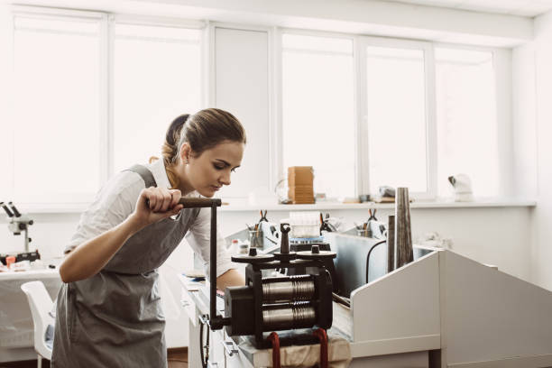 istock Raw material processing. Female woman goldsmith crafting metal on craft rolling machine 1132088915