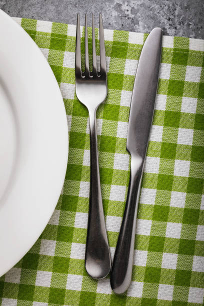 istock Cutlery on the table with a green napkin and a white ceramic plate, top view 1132089101