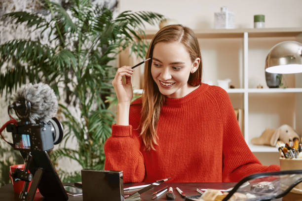 istock Eyebrows modeling. Smiling and young blogger wearing red sweater modeling her eyebrows while recording tutorial video 1132090248
