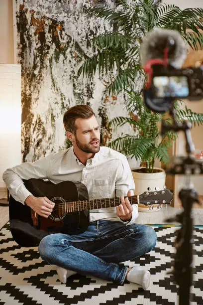 Photo of Famous singer. Bearded male music blogger playing the guitar and singing, while recording new video for his subscribers.