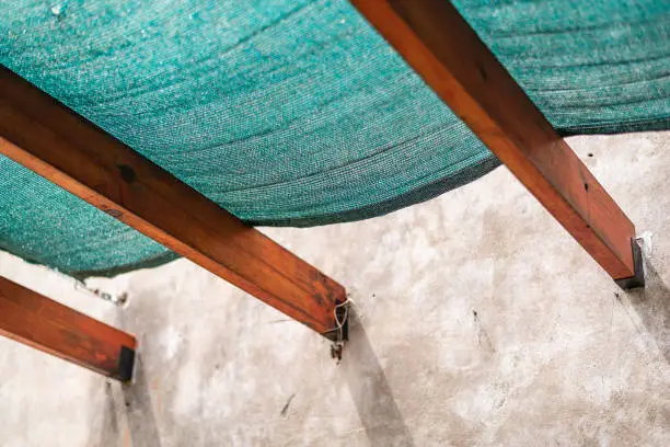 Photo of A plastic sun protection mesh on wooden beams and a cracked concrete wall