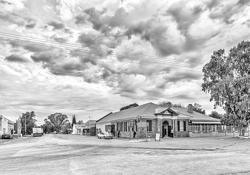 Carnavon, South Africa, September 1, 2018: An early morning street scene, with a bank building and houses, in Carnavon in the Northern Cape Province. Vehicles and people are visible. Monochrome