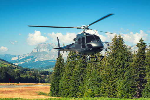 Dark color helicopter landing in beautiful french Alps landscape in small altitude airport of Megeve in summer