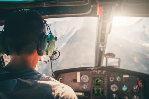 Photo of Helicopter cockpit with rear view of unrecognizable men co-pilot flying over Mont Blanc massif in French Alps mountains at sunset