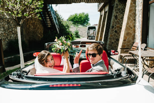 счастливый жених и невеста, молодожены свадебная пара ведет ка�бриолет ретро автомобиль с воздушными шарами на промех на медовый месяц посл - newlywed wedding couple human hair стоковые фото и изображения