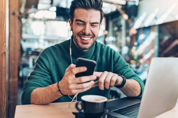 istock Smiling man with smart phone and laptop in cafe 1132102632