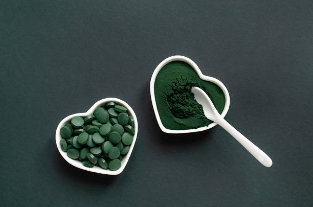 스 피 룰 리 나 파우더와 세라믹 스푼이 있는 하트 모양 그릇에 정제 - spirulina bacterium green vitamin pill medicine 뉴스 사진 이미지