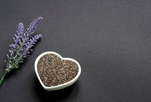 Salvia hispanica chia seeds on dark background with flowers Salvia hispanica chia seeds rich in fiber and omega fatty aicds. Placed in a beautiful white heart shaped bowl and flower decoration. Copy space. salvia hispanica plant stock pictures, royalty-free photos & images