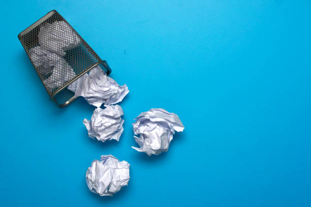 istock White crumpled paper balls rolling out of a trash can. 1132115837