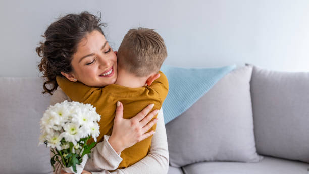 figlio che abbraccia la madre felice con i fiori. - mothers day mother kissing child foto e immagini stock