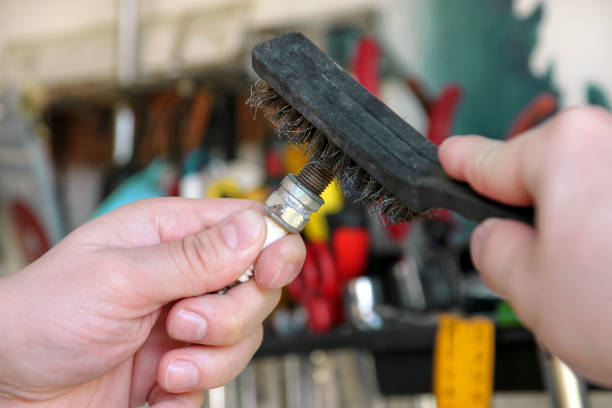 cleaning a car engine spark plug with wire brush in car garage. mechanic is brushing used spark plug with a stainless steel brush in auto mechanics workshop. worker with service tools in hand. - spark plug electrode transportation workshop imagens e fotografias de stock