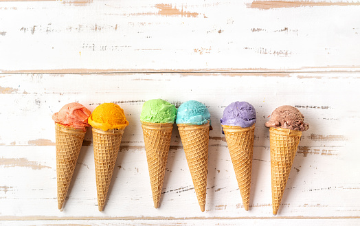 Top view of colorful rainbow ice cream cones on white wooden backgound. Summer concept