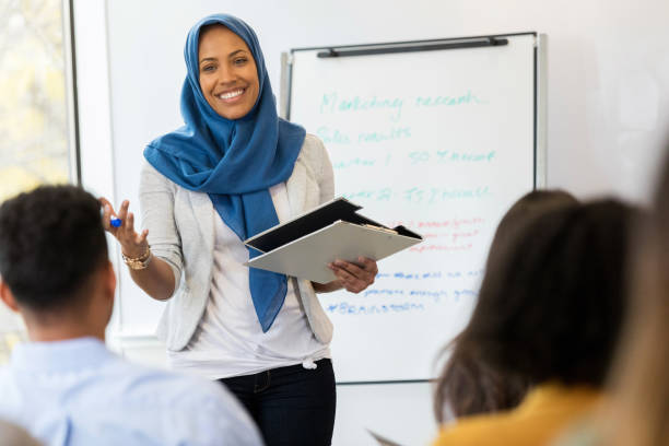 Businesswoman conducts employee training class A mid adult Muslim businesswoman smiles as she speaks to a group of employees during a training class. hijab photos stock pictures, royalty-free photos & images