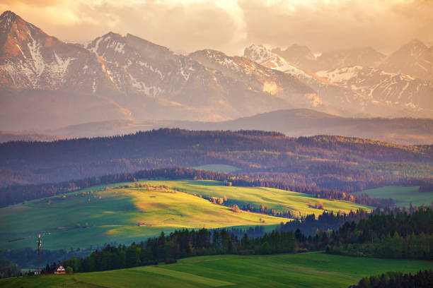 Snow caped mountains and green fields and meadows in Malopolska region, Poland. Spring sunset in Tatra Mountains, Pieniny range