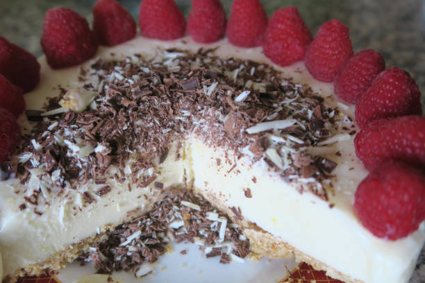 Image of cut gourmet homemade raspberry cheesecake cake dessert with red berries on kitchen worktop