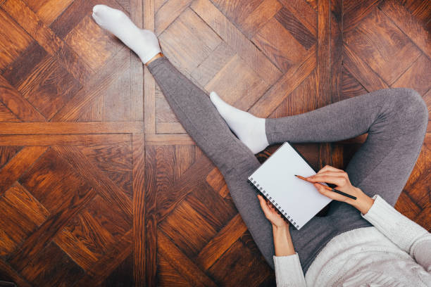 Concept of comfortable work at home Concept of comfortable work at home. View from above woman relaxing sitting on wooden floor writing in notepad. woman legs open stock pictures, royalty-free photos & images