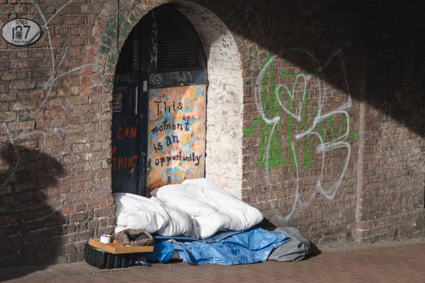 Brighton, United Kingdom. April 23, 2019. This photo, taken under a bridge in Brighton, close to the train station, shows what appears to be a precarious bed made with a blanket and some plastic on the street. Behind, you can find a painting that says \