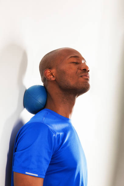 Mature bald black man using rubber ball to massage his neck against a wall Mature bald black man using rubber ball to massage his neck against a wall. He is wearing a blue sports t-shirt. black male massage stock pictures, royalty-free photos & images
