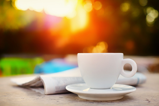 Morning coffe or tea in a white cup and a newspaper with beautiful glowing  bokeh at the background