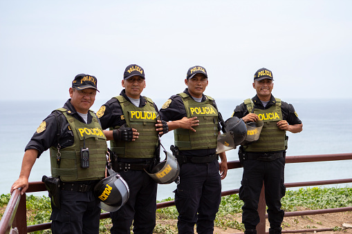 Lima, Peru - February 17 2019: Four friendly Peruvian police men wearing uniforms and green vests smiling in Miraflores, Costa Verde, nature and ocean background