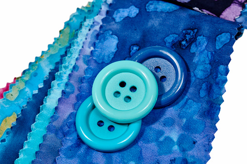 Multi-colored remnants of fabric  with large colorful buttons laying on top isolated on white