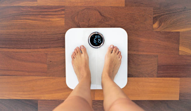Woman bare feet standing on a digital scale with body fat analyzer Top view of woman bare feet standing on a digital scale with body fat analyzer that uses bioelectrical impedance (BIA) to gauge the amount of fat in your body weight scale photos stock pictures, royalty-free photos & images