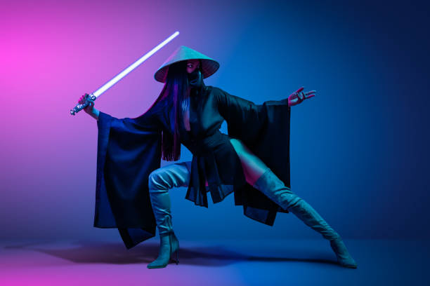 Concept on cosmic cosplay. Concept on cosmic cosplay. Сontemporary portrait a young athletic woman in traditional Japanese black kimono, an Asian hat and highboots is holding a lightsaber and posing on neon blue-pink background cosplay event stock pictures, royalty-free photos & images