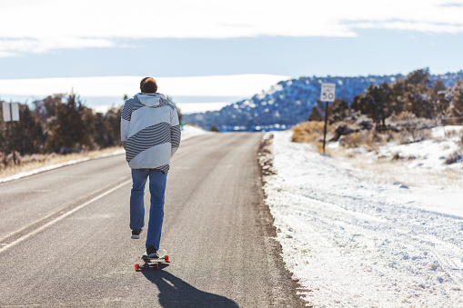 Mature Adult Dominican Male Riding a Longboard on an Outdoor Adventure of Fun Travel in Western Colorado Outdoor Snowy Mountains in the Colorado National Monument Park (Shot with Canon 5DS 56mp photos professionally retouched - Lightroom / Photoshop - original size 5792 x 8688)
