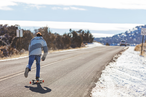Mature Adult Dominican Male Riding a Longboard on an Outdoor Adventure of Fun Travel in Western Colorado Outdoor Snowy Mountains in the Colorado National Monument Park (Shot with Canon 5DS 56mp photos professionally retouched - Lightroom / Photoshop - original size 5792 x 8688)