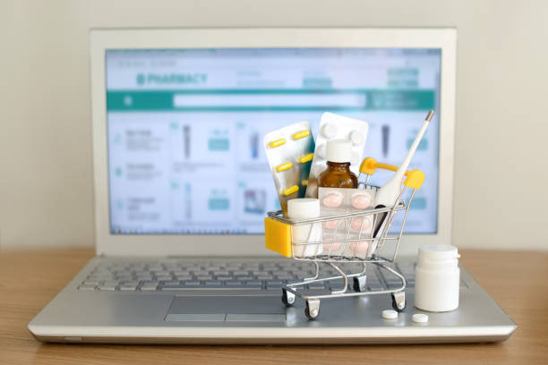 shopping cart toy with medicaments in front of laptop screen with pharmacy web site on it. pills, blister packs, medical bottles, thermometer set. health care and internet shopping. - hardware store fotos imagens e fotografias de stock