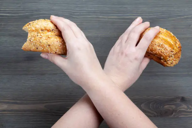 First-person view of the bitten bread in crossed arms at dark wooden background. Dietary concept. Copy space