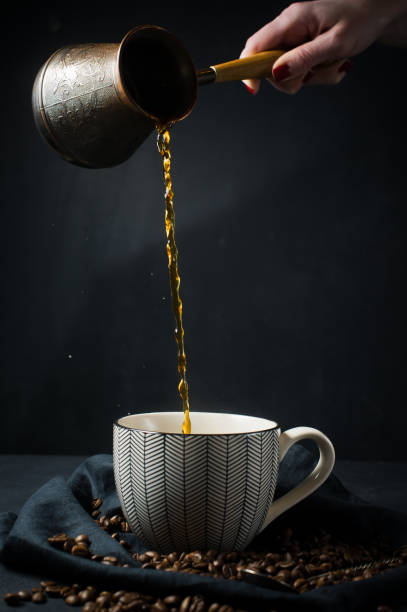 A woman's hand pours coffee from the Turks in a Cup. Black background, top view, space for text.