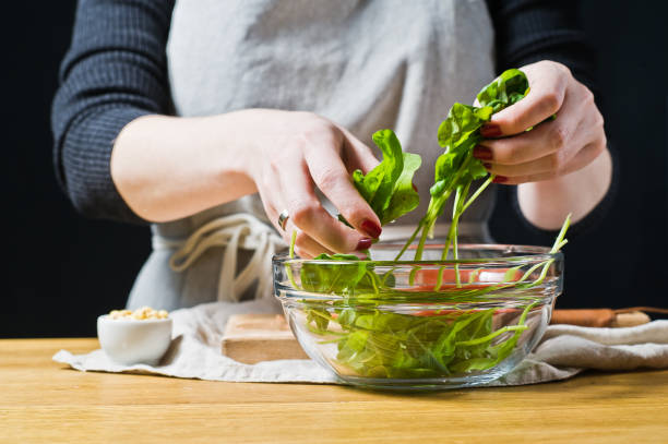 istock Chef puts arugula leaves in a bowl, preparing a salad. Black background, side view, kitchen. 1132191884