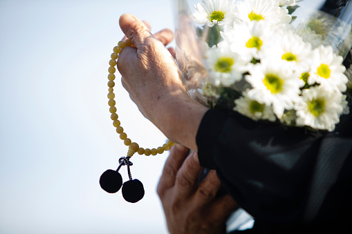 An item of the ceremony of the funeral of Japan. The Japanese woman of the senior in the black mourning dress which went for a visit to a grave with a chrysanthemum bunch and beads.