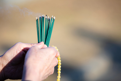 An item of the ceremony of the funeral of Japan, an incense stick.\n\nThe Japanese woman of the senior to hold an exiting incense stick of the smoke in a hand in a black mourning dress.