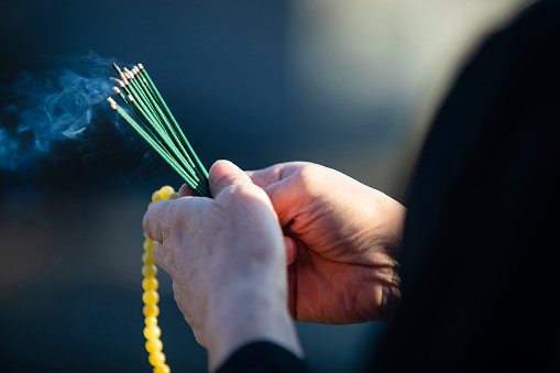 An item of the ceremony of the funeral of Japan, an incense stick.\n\nThe Japanese woman of the senior to hold an exiting incense stick of the smoke in a hand in a black mourning dress.