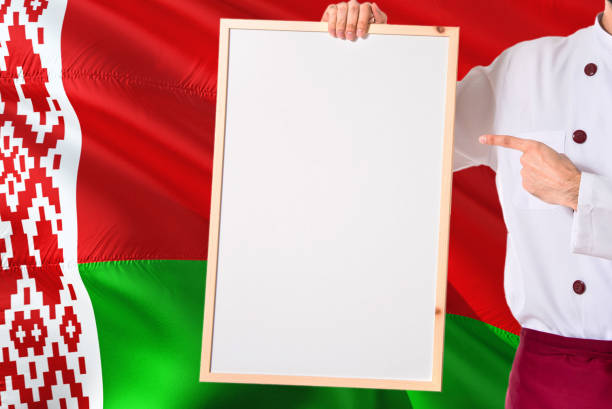 Belarusian Chef holding blank whiteboard menu on Belarus flag background. Cook wearing uniform pointing space for text.